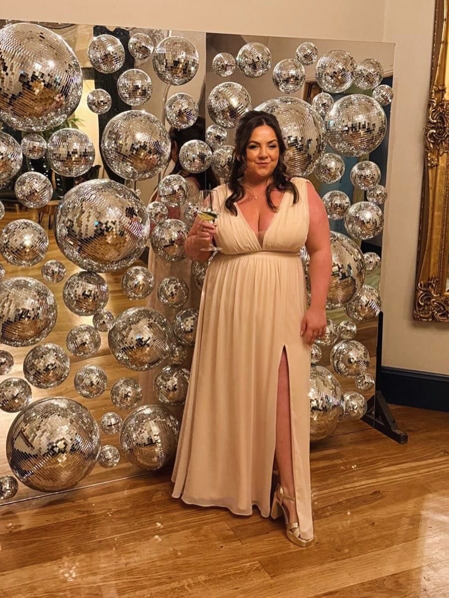A customer in a cream occasion dress against a mirror-ball backdrop
